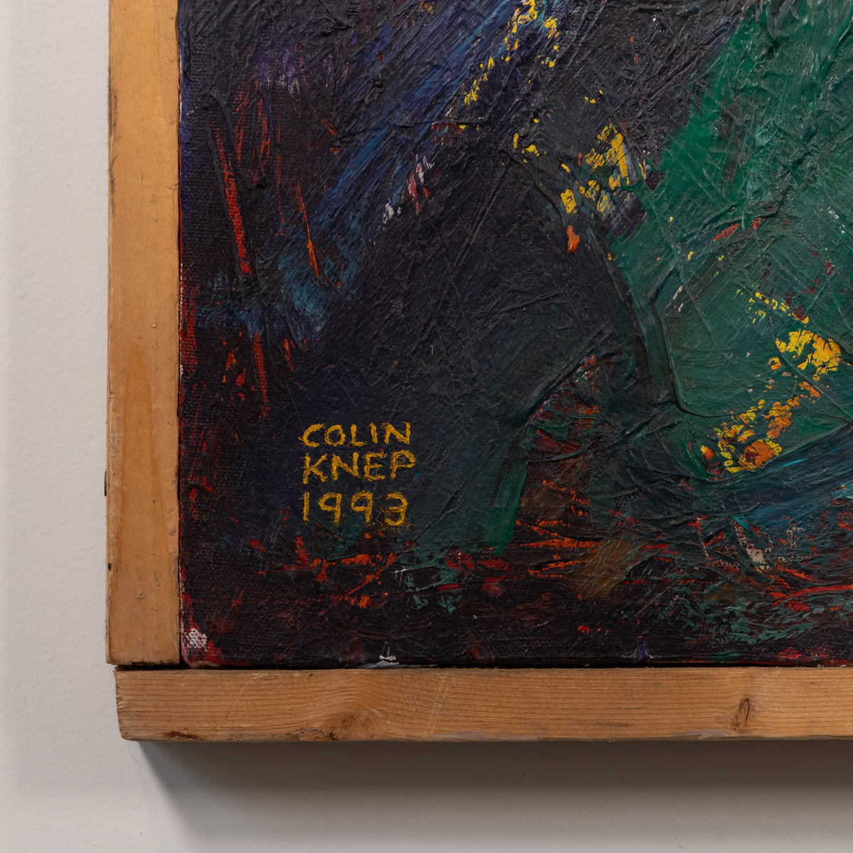 Close-up of an abstract painting showing thick textured brushstrokes in black, green, blue, red, and yellow, with a wooden frame edge and the signature 'COLIN KNEP 1993' visible.