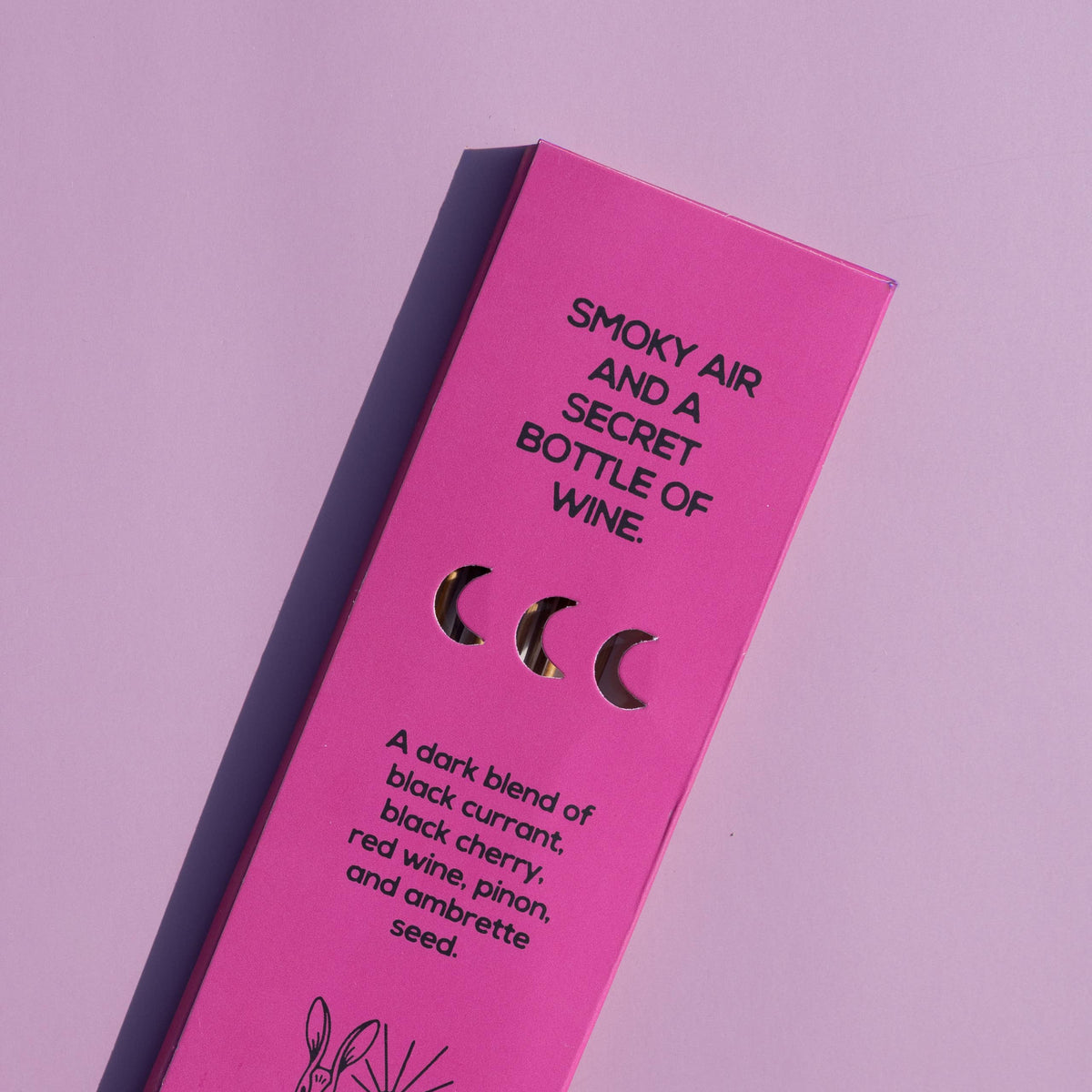 Bright pink rectangular product packaging for Brass Earth wine, photographed at an angle on a matching pink background. The box features black text reading 'SMOKY AIR AND A SECRET BOTTLE OF WINE.