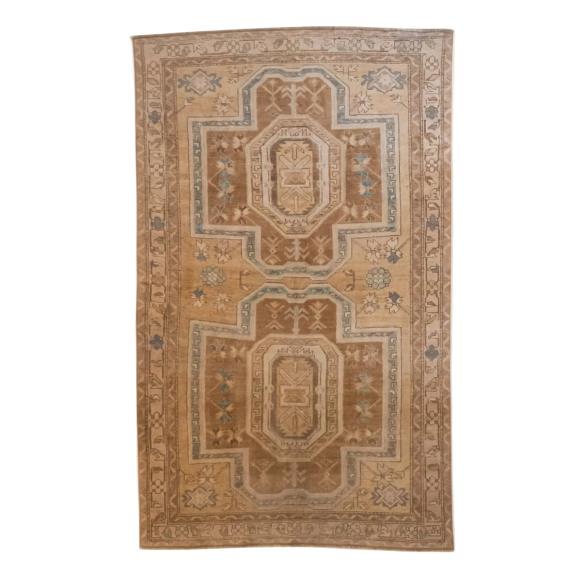 A rectangular vintage-style area rug with a traditional geometric medallion pattern in warm tan, beige, and brown tones with muted blue accents, shown flat against a plain white background.