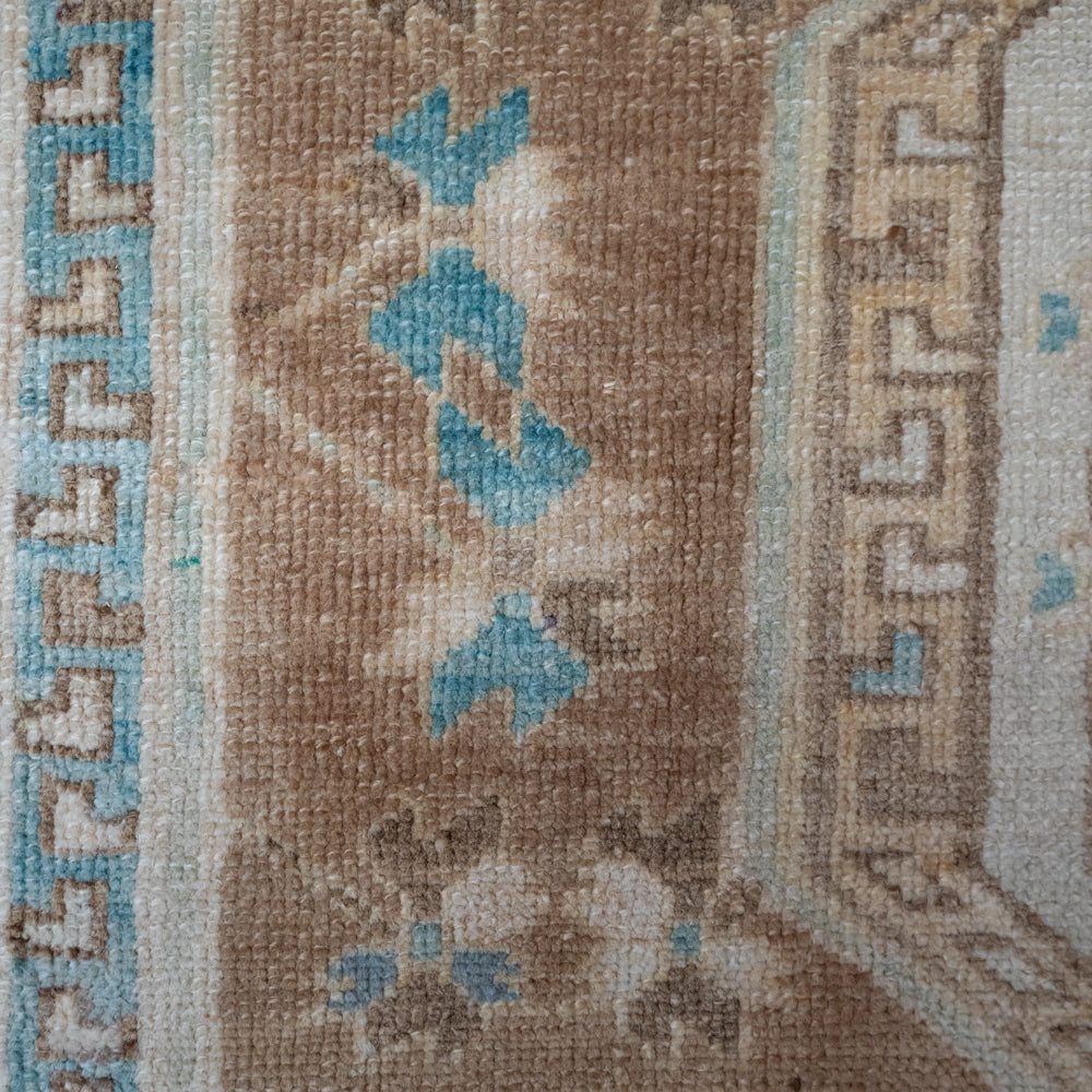 A close-up of a vintage-style rug featuring a distressed brown field with light blue and beige geometric motifs and borders.