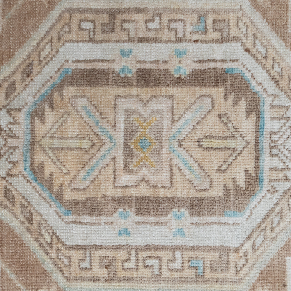 A close-up of a woven textile or rug pattern with an octagonal medallion design in beige, brown, cream, light blue, and small yellow accents.