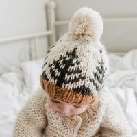 Baby wearing a knitted hat with a pom-pom on a bed