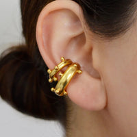 A close-up of a person's ear wearing a chunky, multi-band gold ear cuff with small bead details.
