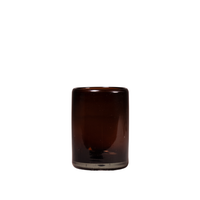 A small cylindrical amber glass tumbler with a thick base, shown against a plain white background.