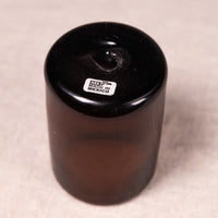 A small cylindrical dark brown glass bottle with a black screw-on cap, featuring a small white 'MADE IN MEXICO' label on the cap, set against a neutral beige background.