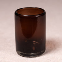 A small cylindrical amber brown glass tumbler or candle holder, photographed on a neutral beige fabric background.