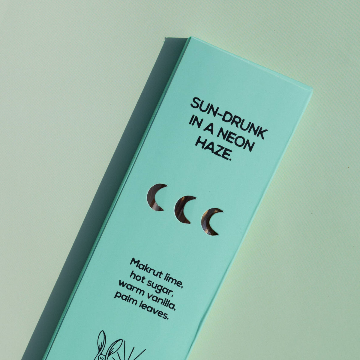 A mint green rectangular product box for Brass Earth, photographed at an angle on a matching mint background. The box features black text reading 'SUN-DRUNK IN A NEON HAZE.