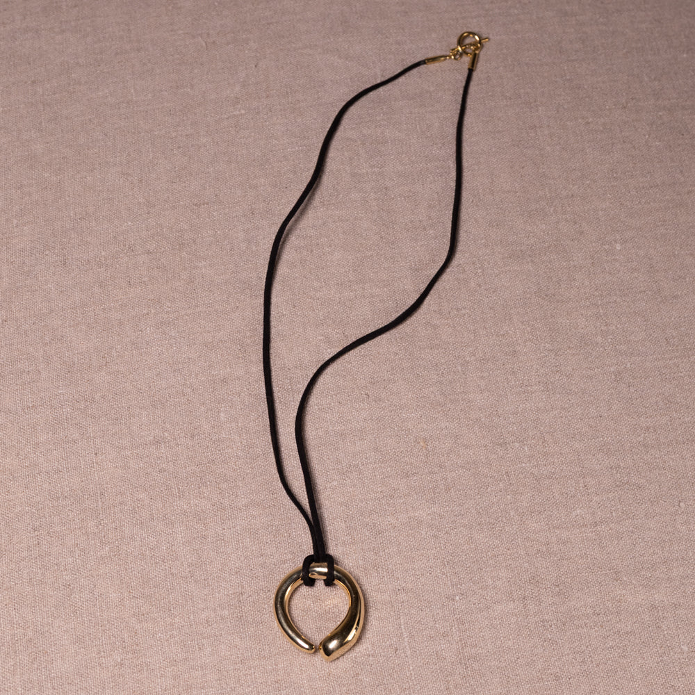 A gold heart-shaped pendant necklace on a black cord, displayed on a textured beige linen background.