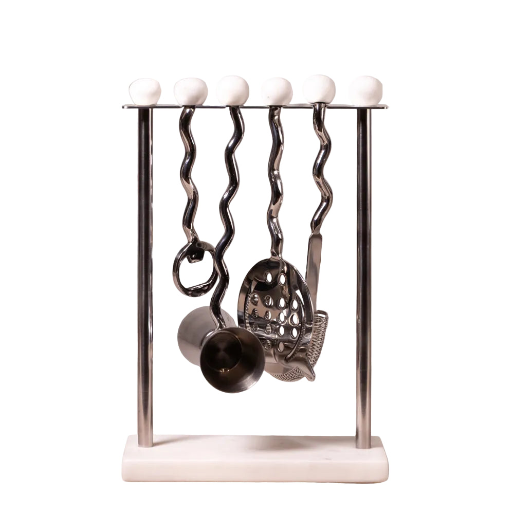 A kitchen utensil rack with a polished metal stand, six wavy hanging handles, and white spherical finials along the top bar. Several utensils, including a whisk, strainer, and measuring cup, are hanging from the stand against a light textured wall background.