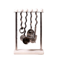 A kitchen utensil rack with a polished metal stand, six wavy hanging handles, and white spherical finials along the top bar. Several utensils, including a whisk, strainer, and measuring cup, are hanging from the stand against a light textured wall background.