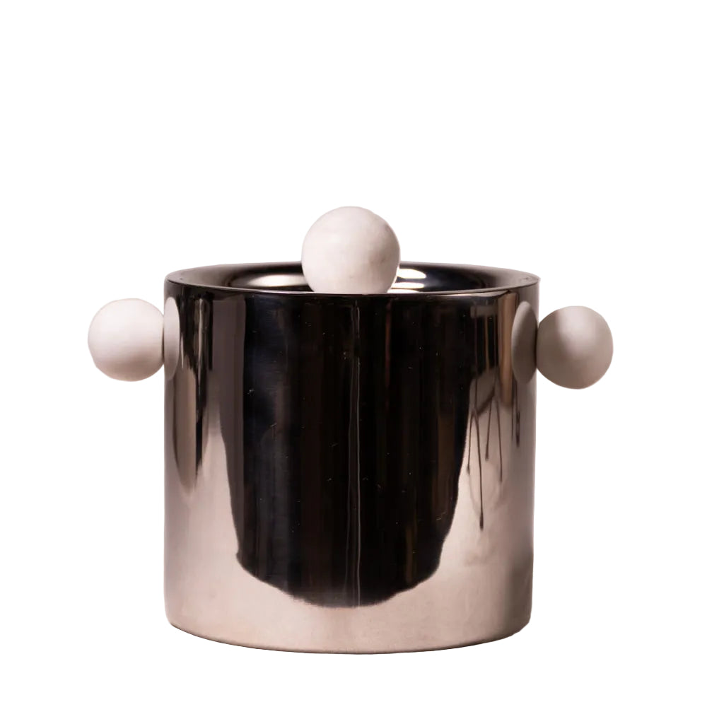 A modern cylindrical metal container with a reflective silver finish, featuring three matte white spherical protrusions (one on top and two on the sides), set against a textured light beige background.