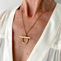 Gold necklace with a unique pendant worn by a person in a white outfit.