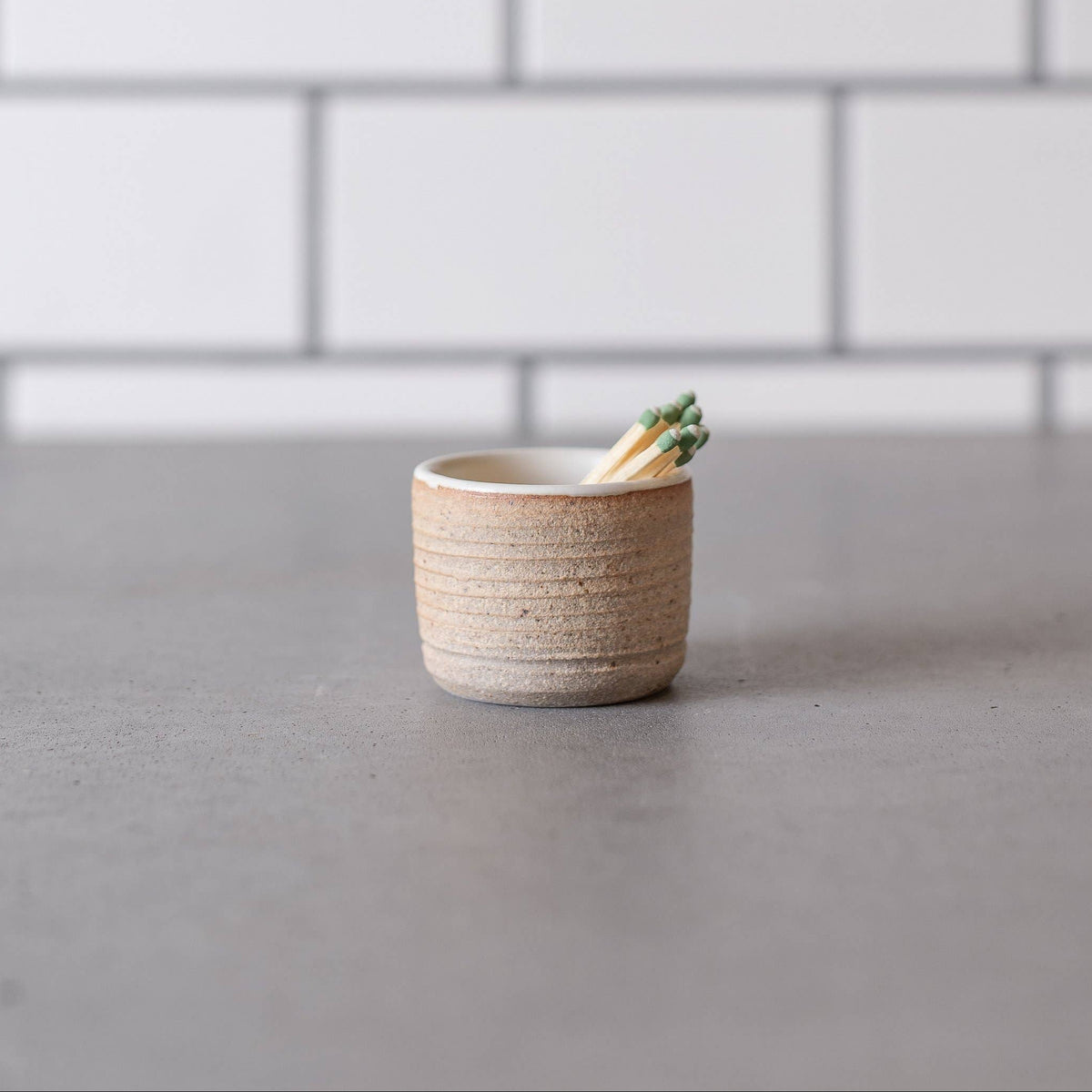 Small ceramic cup with a plant on a gray surface against a white tiled wall.