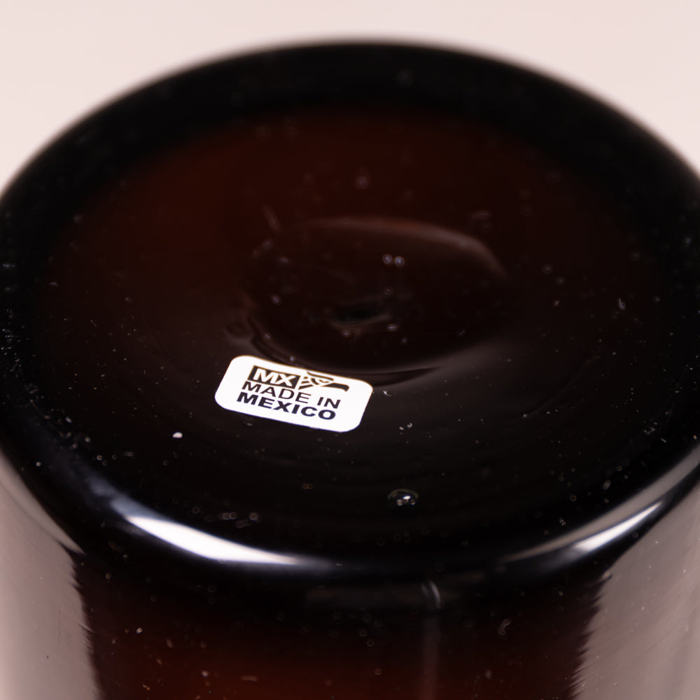 Close-up of the bottom of a dark brown glass vessel, showing a glossy finish, tiny air bubbles, and a white 'MADE IN MEXICO' sticker.
