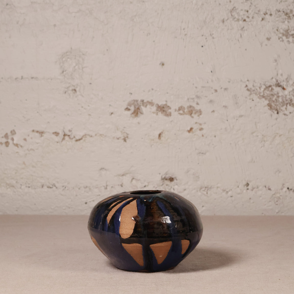 Small ceramic vase with black and gold design on a textured surface