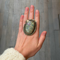 Hand wearing a large, ornate ring with a stone on a neutral background