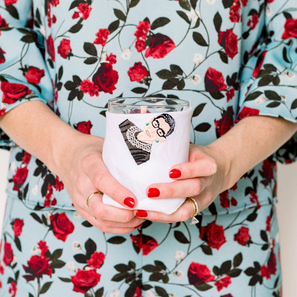 Person holding a white tumbler with a design, wearing a floral dress.