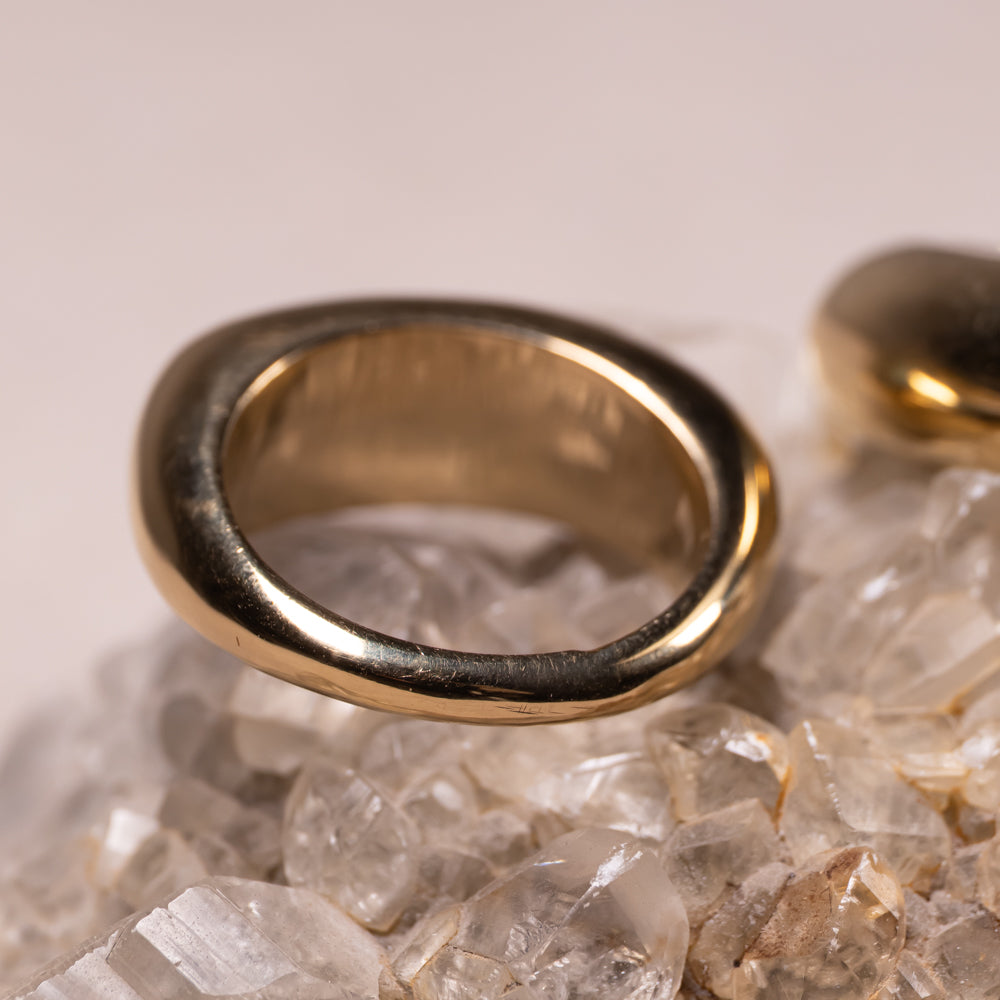A thick, polished gold ring with a textured, organic outer surface, resting on a bed of clear quartz crystals.