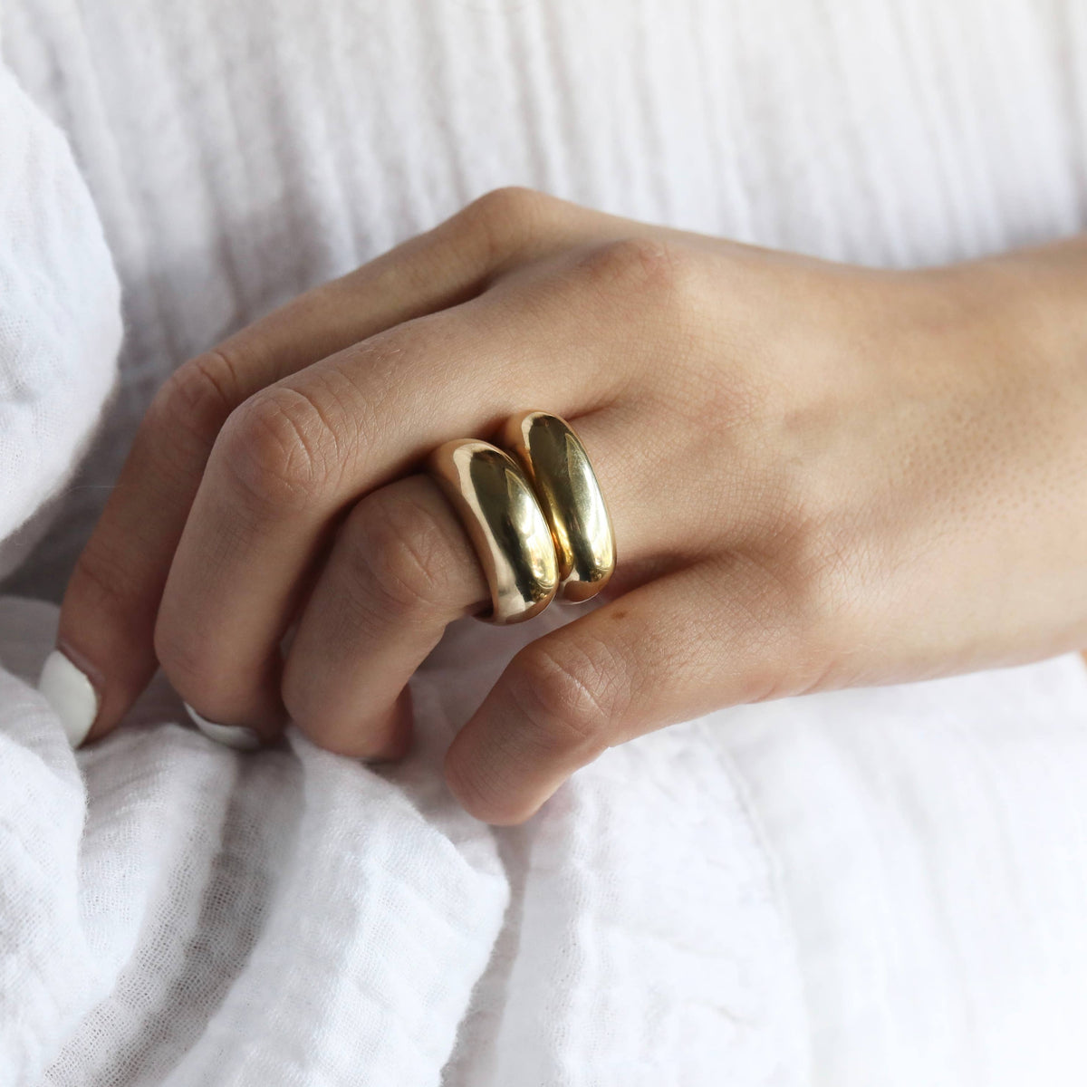 Hand wearing a gold ring on a white fabric background