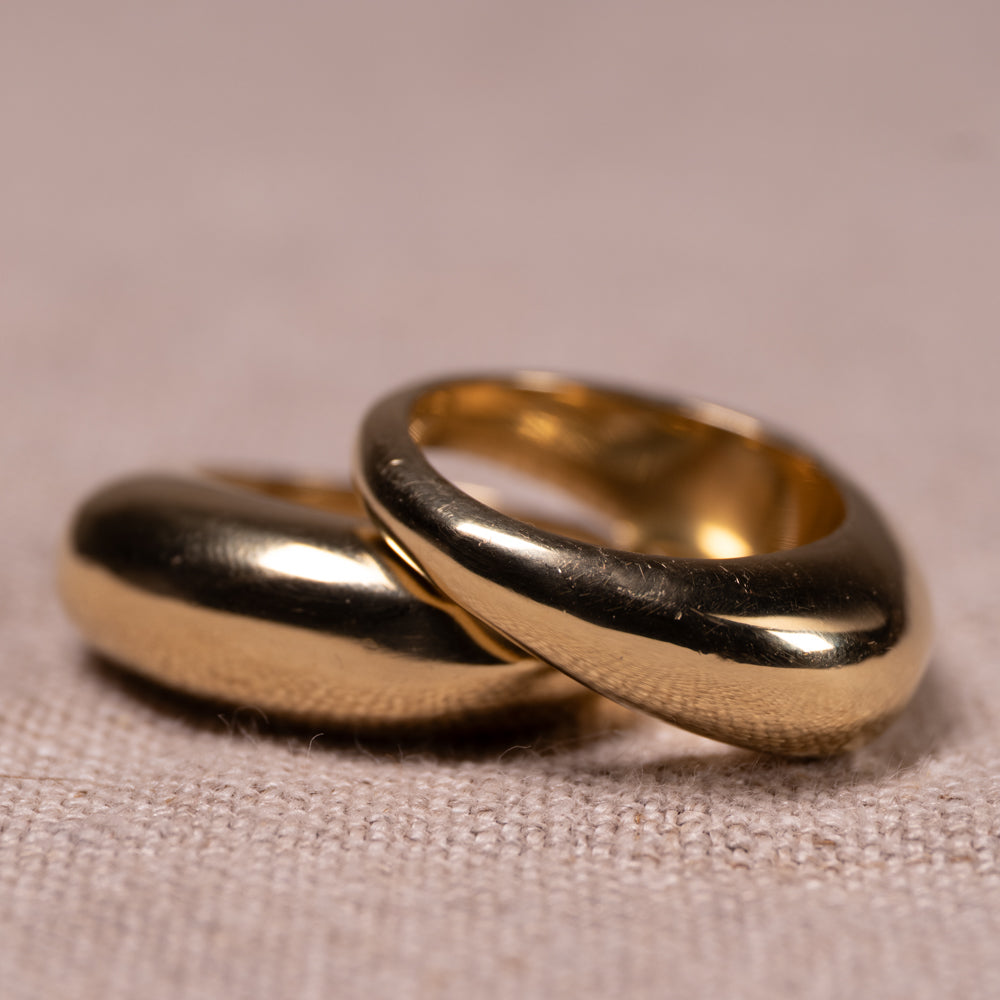Two overlapping matte gold rings resting on a textured beige fabric surface.