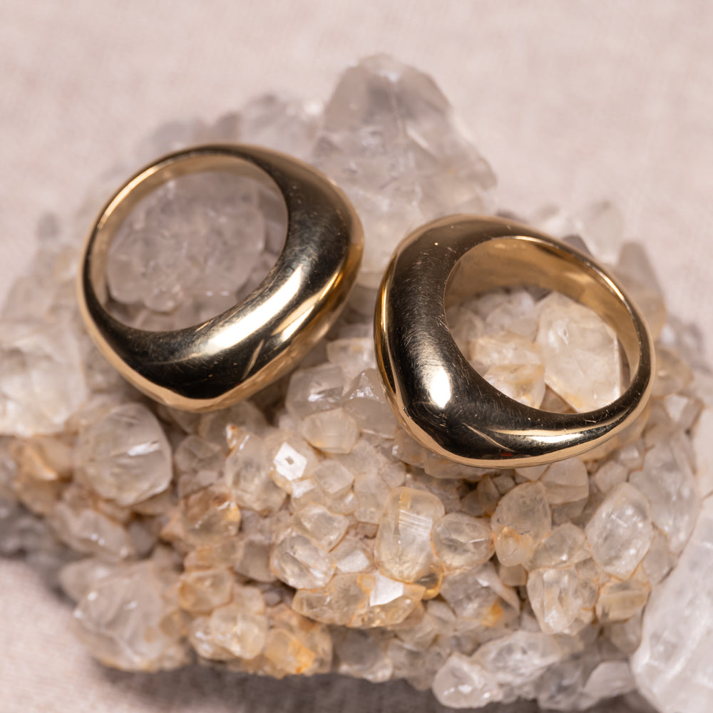 Two gold-toned chunky ring earrings displayed on a bed of clear quartz crystals against a neutral beige background.