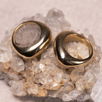Two gold-toned chunky ring earrings displayed on a bed of clear quartz crystals against a neutral beige background.
