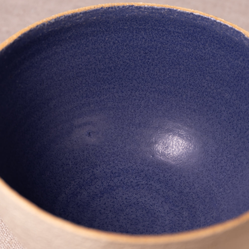 Close-up of the interior of a ceramic bowl with a deep navy blue glaze and a natural beige clay rim.
