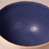 Close-up of the interior of a ceramic bowl with a deep navy blue glaze and a natural beige clay rim.