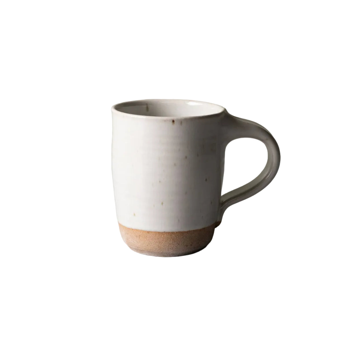 A handmade ceramic mug with a matte off-white body, a textured light brown base, and a curved handle, set against a neutral gray surface and a textured light green wall.